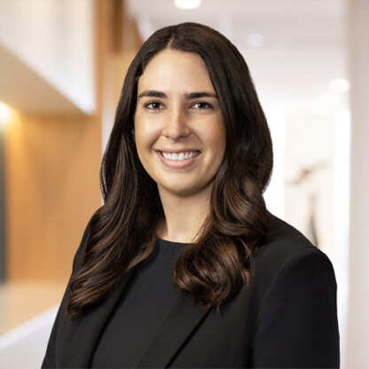 A woman with long brown hair, wearing a black blazer, smiles at the camera in a modern office setting, representing lawyers in Chicago who specialize in intellectual property law.