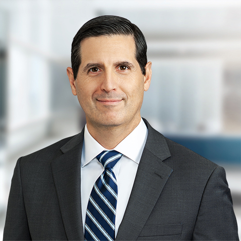 A man in a dark suit and striped tie stands in front of a blurred corporate law office, looking at the camera with a neutral expression—reflecting the professionalism of top Chicago lawyers.