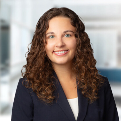 Woman with long curly brown hair wearing a dark blazer and white top, smiling at the camera in a brightly lit law offices setting, representing litigation support professionals in Chicago.
