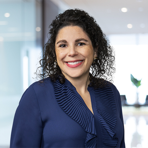 Woman with curly dark hair wearing a navy blouse, smiling in a modern office setting with glass walls—perfect for chicago lawyers specializing in litigation support and intellectual property law.