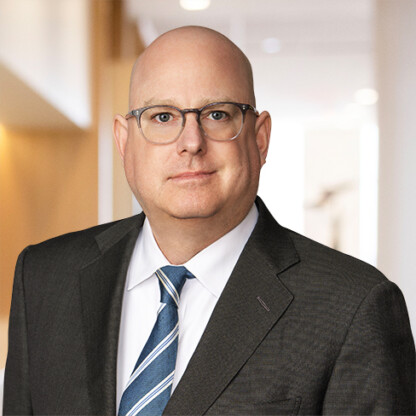 A bald man wearing glasses, a dark suit, white shirt, and striped tie stands in a well-lit corporate law office hallway, embodying the professionalism of top lawyers in Chicago.