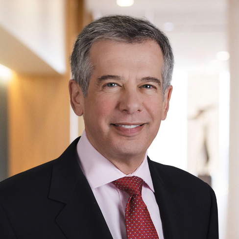 A middle-aged man with short gray hair, wearing a dark suit, light pink shirt, and red patterned tie, stands indoors with a blurred office background—ideal for profiles of litigation support specialists or Chicago lawyers.