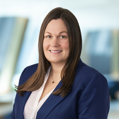 A woman with long brown hair, wearing a navy blazer over a white blouse, smiles at the camera in a modern corporate law office, reflecting the professionalism of top lawyers in Chicago.