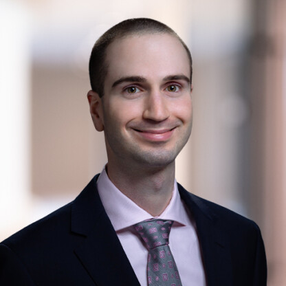A man in a suit and pink tie smiles at the camera against a blurred indoor background, reflecting the professionalism of Chicago lawyers.