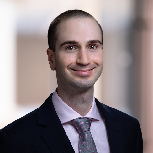 A man in a suit and pink tie smiles at the camera against a blurred indoor background, reflecting the professionalism of Chicago lawyers.
