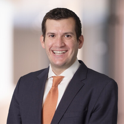 A man in a dark suit and orange tie, specializing in litigation support, smiles at the camera against a blurred indoor background.