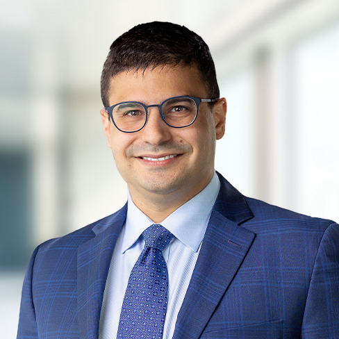 A man with short dark hair and glasses wearing a blue suit, light blue shirt, and patterned tie, standing in a brightly lit indoor setting, represents chicago lawyers specializing in intellectual property law.
