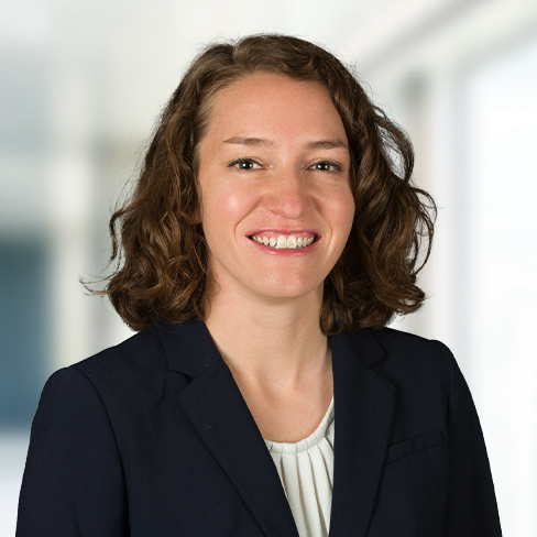 A woman with shoulder-length curly brown hair, wearing a dark blazer and light blouse, smiles at the camera in a brightly lit law office offering litigation support for Chicago lawyers.