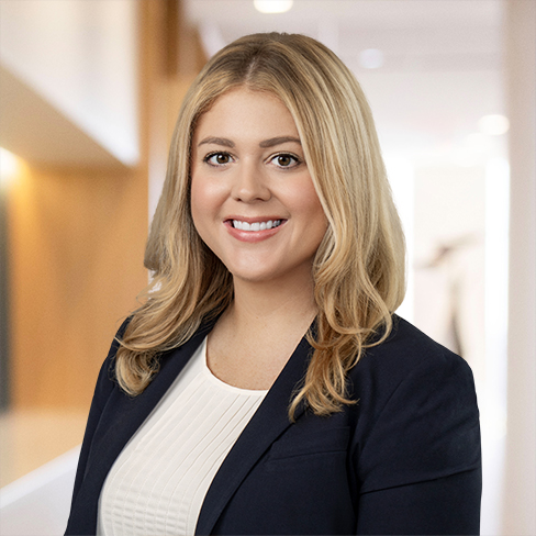 A woman with long blonde hair, wearing a navy blazer and white top, smiles in a brightly lit corporate law office, reflecting the professional atmosphere of lawyers in Chicago.