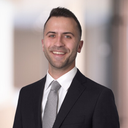 A man in a dark suit, white shirt, and patterned tie is smiling while standing in front of a blurred indoor background, reflecting the professionalism often seen among lawyers in Chicago.