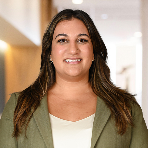 A woman with long brown hair wearing a light green blazer and white top stands indoors, smiling at the camera in one of the top law offices specializing in intellectual property law.