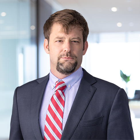 A man in a suit and red striped tie stands in a modern law office with glass walls, representing top lawyers in Chicago amid blurred background elements.