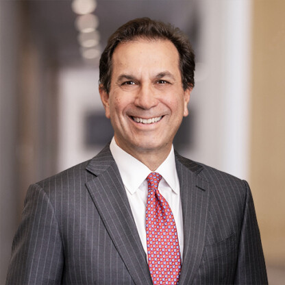 A man in a gray pinstripe suit, white shirt, and red patterned tie smiles while standing in the well-lit hallway of a corporate law office.