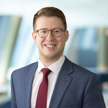 A man wearing glasses, a suit, white shirt, and red tie is smiling in front of a blurred corporate law office background, reflecting the professionalism of Chicago lawyers.