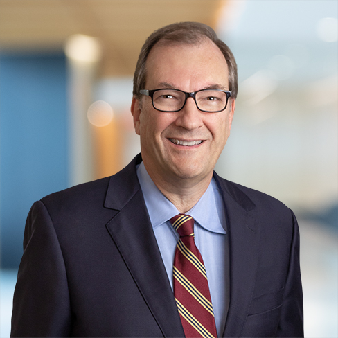Man wearing glasses, a dark suit, blue shirt, and striped tie, smiling in a modern corporate law office with a blurred background—ideal representation of top lawyers in Chicago.