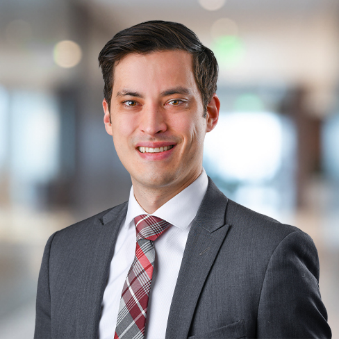 A man in a gray suit, white shirt, and plaid tie is smiling at the camera in a blurred corporate law office, reflecting the professionalism of chicago lawyers.
