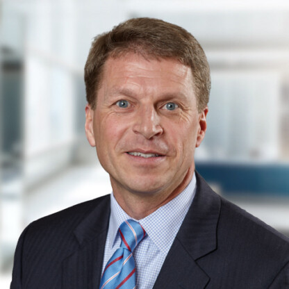 Middle-aged man in a suit and striped tie smiling, posed in a modern law office setting—an ideal professional for litigation support or intellectual property law.