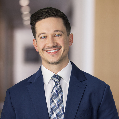 Man in a blue suit and plaid tie smiling, standing in a modern office hallway with blurred background, representing experienced lawyers in Chicago.