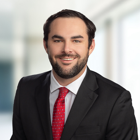 A man in a black suit, white shirt, and red tie smiles at the camera against a blurred indoor background, reflecting the professional image often seen at top Chicago law offices.