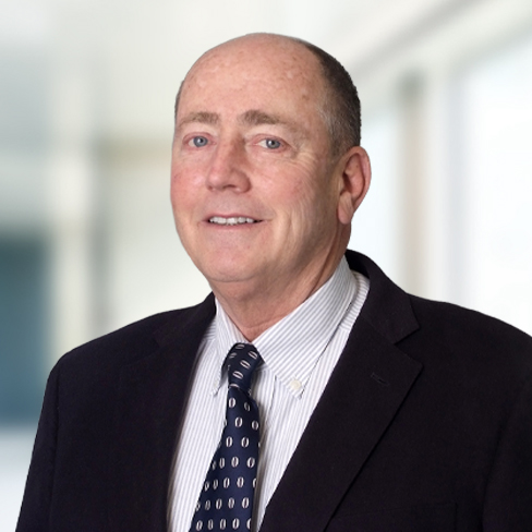 A middle-aged man with short hair wearing a dark suit jacket, striped shirt, and patterned tie stands against a blurred indoor background, representing experienced lawyers in Chicago at a leading corporate law office.