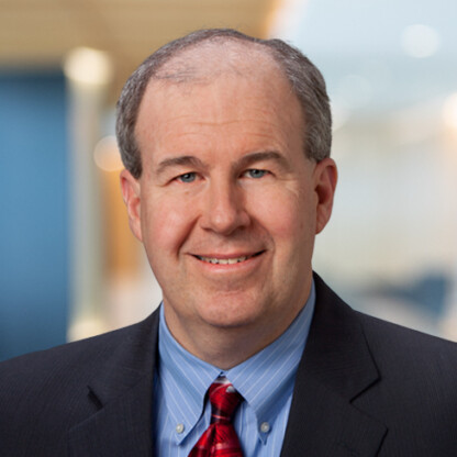 A middle-aged man in a suit and red tie smiles at the camera in an office setting with a blurred background, reflecting the professionalism of lawyers in Chicago who specialize in intellectual property law.