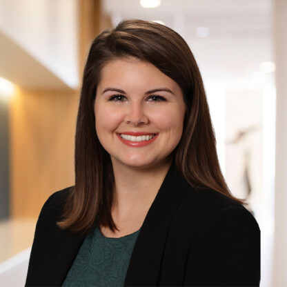 A woman with straight brown hair, wearing a dark blazer and green top, smiles at the camera in a well-lit corporate law office, reflecting the professional environment of lawyers in Chicago.