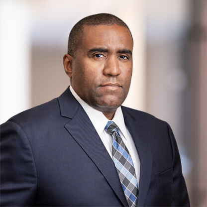 A man in a dark suit, light shirt, and patterned tie stands against a blurred background, looking directly at the camera with a neutral expression—reflecting the professionalism of leading law offices and lawyers in Chicago.