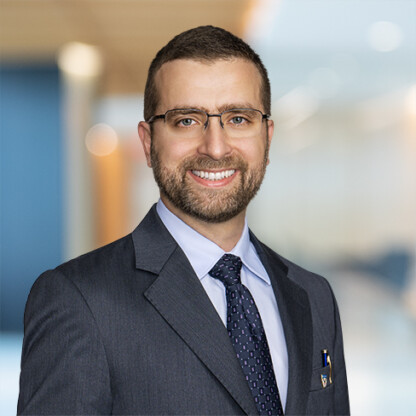 A man in a suit and tie with glasses smiles at the camera in a modern law office, reflecting his expertise in intellectual property law.