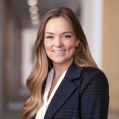 A woman with long blonde hair wearing a navy plaid blazer and white blouse smiles in a softly lit hallway, exemplifying the approachable professionalism of top Chicago lawyers.