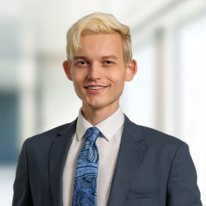 A young man with short blond hair wearing a dark suit, white shirt, and blue patterned tie stands in a brightly lit law offices setting alongside experienced Chicago lawyers.