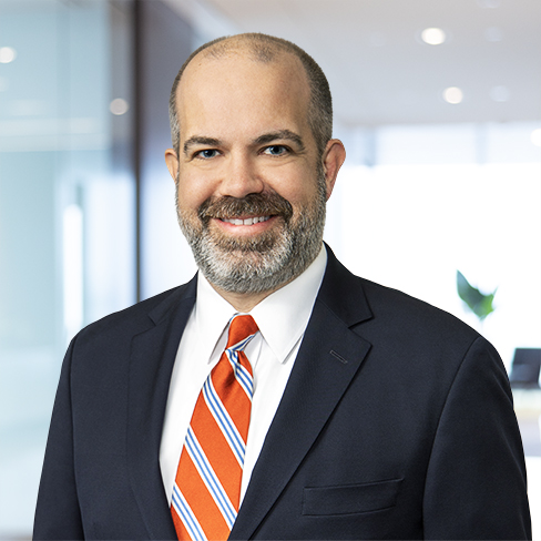 A man in a suit and striped tie stands in a modern office setting, smiling at the camera—representing one of the top law offices offering litigation support and experienced lawyers in Chicago.