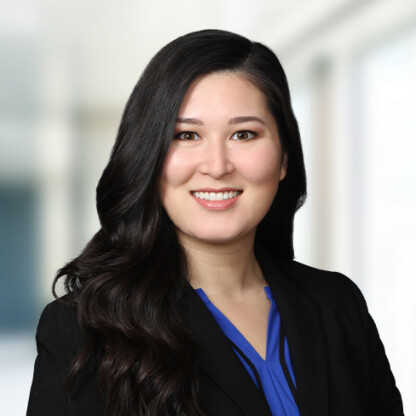 A woman with long dark hair, wearing a black blazer and blue blouse, smiles at the camera in a brightly lit, blurred office—embodying the professionalism of chicago lawyers specializing in intellectual property law.