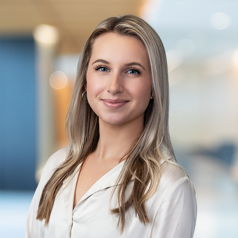 Woman with long blonde hair wearing a cream blouse, standing indoors with a blurred law offices background, reflecting the professional environment of lawyers in Chicago.
