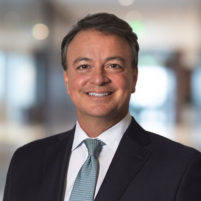 A man in a suit and tie smiles at the camera, standing in a blurred indoor office setting—reflecting the professionalism of lawyers in Chicago.