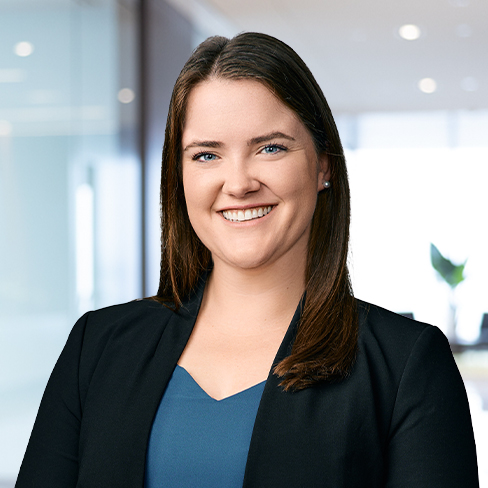 A woman with straight brown hair, wearing a black blazer and blue top, smiles in a modern corporate law office, likely among Chicago lawyers, with a blurred background.