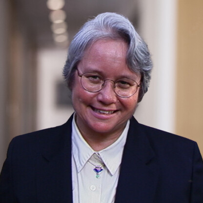 An older person with short gray hair, glasses, and a dark suit smiles while standing in a corridor with blurred lights in the background, reflecting the confidence of seasoned lawyers in Chicago.