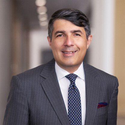 A man in a gray pinstripe suit, white shirt, and patterned tie smiles while standing in a hallway with blurred lights, reflecting the professionalism of Chicago lawyers specializing in litigation support.