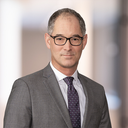 A man wearing glasses and a gray suit with a purple tie stands in front of a blurred indoor background, reflecting the professional atmosphere of law offices and litigation support.