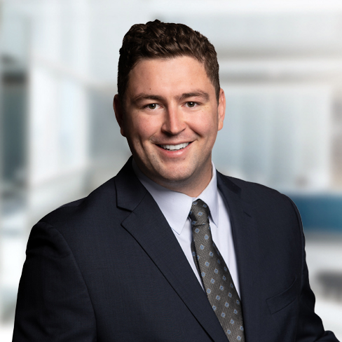 A man in a dark suit and tie smiles at the camera in a professional, modern corporate law office, with blurred background—reflecting the dynamic environment of Chicago lawyers and their commitment to excellence.