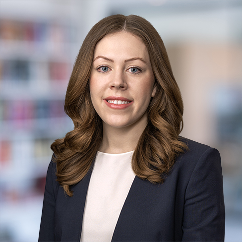 A woman with long brown hair wearing a navy blazer and white top poses against a blurred office background, representing one of the leading law offices specializing in intellectual property law in Chicago.