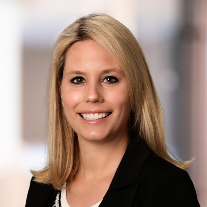 A woman with straight blonde hair wearing a black blazer and white top, smiling at the camera against a blurred indoor background, representing the professionalism of leading Chicago lawyers.