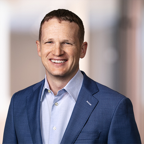 Man in a blue suit jacket and light blue shirt smiling, standing against a blurred indoor background of a corporate law office, representing Chicago lawyers and providing litigation support.