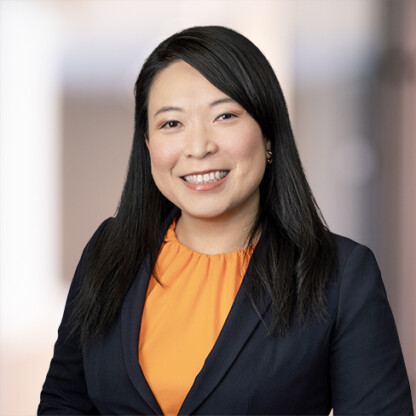 Woman with long black hair wearing an orange blouse and dark blazer, smiling, posed against a blurred indoor background—perfect for representing lawyers in Chicago or a modern corporate law office.
