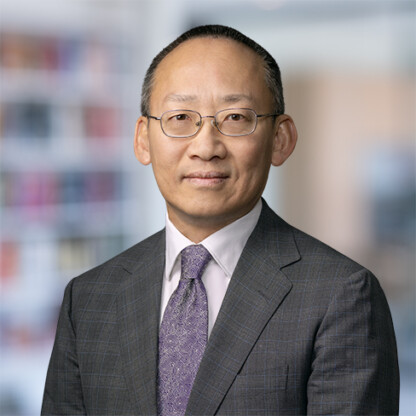 A man wearing glasses and a gray suit with a lavender tie stands in front of a blurred corporate law office, exemplifying the professionalism of Chicago lawyers.