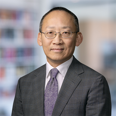 A man wearing glasses and a gray suit with a lavender tie stands in front of a blurred corporate law office, exemplifying the professionalism of Chicago lawyers.