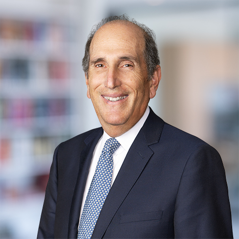 A middle-aged man in a dark suit and patterned tie smiles at the camera, standing in a blurred law office or library setting, reflecting his professionalism in litigation support.