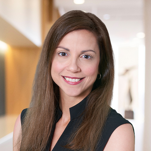 A woman with long brown hair and a black sleeveless top smiles at the camera in a brightly lit corporate law office, reflecting the welcoming atmosphere found among lawyers in Chicago.