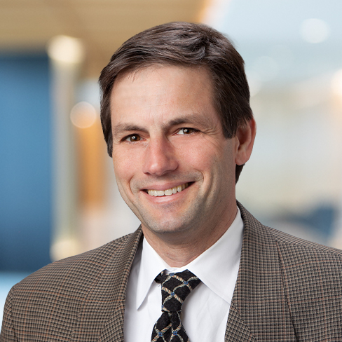 A man in a brown checked suit, white shirt, and patterned tie is smiling in a professional corporate law office, reflecting the distinguished style of top lawyers in Chicago.