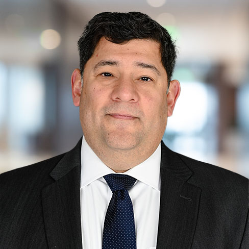 A man wearing a dark suit, white shirt, and dotted navy tie stands in front of a blurred indoor background, reflecting the professionalism found in top Chicago lawyers at a corporate law office.