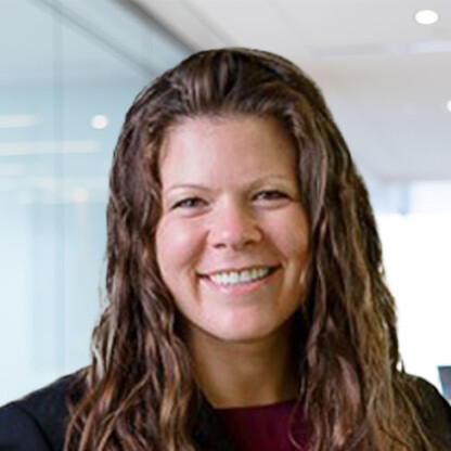 A woman with wavy brown hair and a dark blazer smiles at the camera in a modern, glass-walled corporate law office, exemplifying the professionalism of Chicago lawyers.